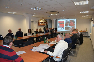 ucestnicy spotkania siedzący przy stole, na ścianie slajdy