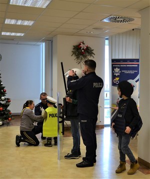policjanci pomajagą dziecim założyć elementy munduru i policyjnego wyposażenia