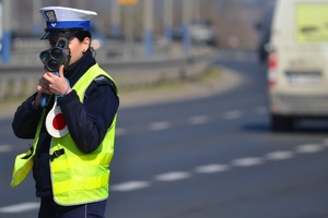 Policjantka ruchu drogowego mierzy prędkość przy drodze ręcznym miernikiem. W tle perspektywa drogi i ruch samochodów