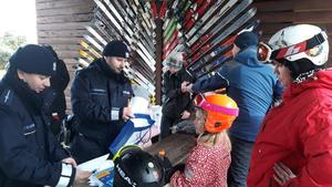 Dzieci z opiekunem stoją na tle wyciągu narciarskiego z upominkami otrzymanymi od Policjantów