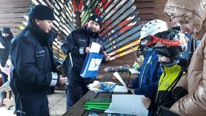 Policjanci rozmawiają z dziecmi na stoku narciarskim i rozdają im ulotki informacyjne o bezpieczeństwie na stoku