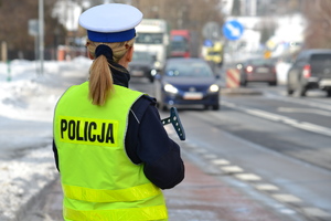 Policjantka ruchu drogowego stoi przy drodze nadzoruje ruch. W tle ruch uliczny i warunki zimowe