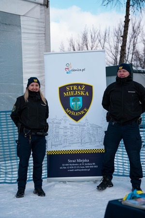 Dwoje umundurowanych strażników miejsckich przed banerem Straży Miejskiej