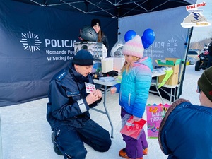 policjant  opowiada stojącej przezd nim małej dziewczynce o numerach alarmowych zapisanych na kolorowej na karteczce