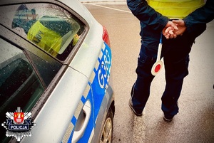 policjant stojący obok radiowozu trzymający tarczę do zatrzymywania pojazdów tzw. lizak.