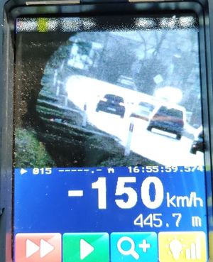 Zdjęcie wyświetlacza ręcznego miernika prędkości z prędkością zmierzoną pojazdu poruszającego się po drodze. Widoczna cyfra (-150 kmh) świadcząca o tym, że pojazd oddalał się od policjantów.