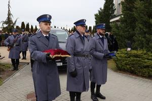 Policjanci niosą czerwoną poduszkę z medalem i czapkę policyjną