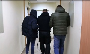 dwóch kryminalnych prowadzi osobę zatrzymaną przez korytarz policyjnego aresztu