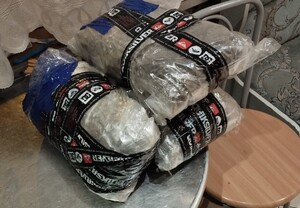 Na zdjęciu położonym na metalowym blacie stołu położone są trzy pakunki owinięte przeźroczysta filią i czarnymi taśmami.