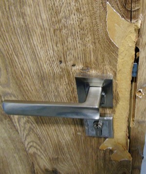 Uszkodzone drzwi wejściowe do mieszkania na wysokości klamki
