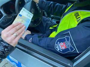 kobieta podająca dowód rejestracyjny i 200 zł policjantowi siedzącemu w radiowozie