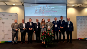 Grupa osób wyróżnionych odznaką honorową zasłużony dla Transportu Rzeczypospolitej Poliskiej, stoją na scenie