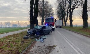 Rozbity samochód na drzewie, za nim pojazd straży pożarnej