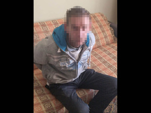 sprawca rozboju siedzi na kanapie skuty kajdankami z tyłu