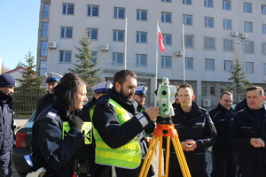 Policjanci omawiają zasadę obsługi urządzenia do laserowego pomiaru punktów z miejsca wypadku drogowego