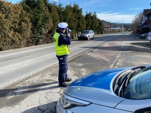 umundurowany policjant mierzący prędkość kierujących przy oznakowanym radiowozie