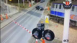 stojący za rogatkami czarny samochód i przejeżdzający obok pociąg