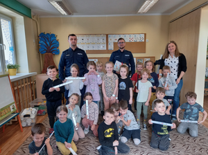 Umundurowani policjanci, wychowawca oraz przedkoszlaki z otrzymanymi wcześniej elementami odblaskowymi