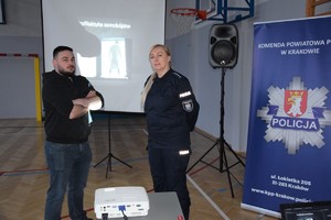 policjantka w mundurze obok policyjny psycholog, stoją przodem do zdjęcia, za nimi ekran z prezentacją, obok baner KPP Kraków