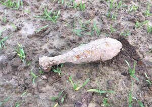 Pocisk moździerzowy o długości około 30 cm i średnicy około 8 cm leżący na polu uprawnym