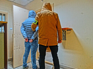 nieumundurowany policjant prowadzi zatrzymanego wewnątrz budynku krynickiego komisariatu - zdjęcie ilustracyjne