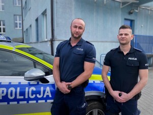 Dzielnicowi mł. asp. Bartosz Gorczyca i mł. asp. Krystian Biela na tle oznakowanego radiowozu i budynku komendy