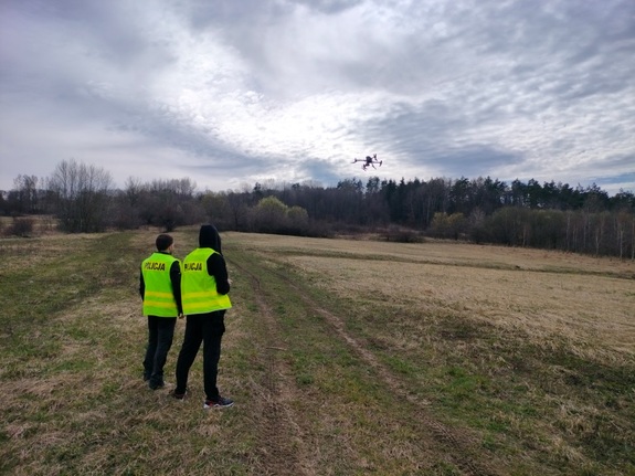 Dwóch policjantów obserwuje z latającego drona tereny łąk i lasów narażone na podpalenia.