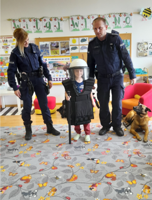 Policjanci, policyjny pies służbowy oraz przedszkolak ubrany w policyjną kamiezelkę oraz kask
