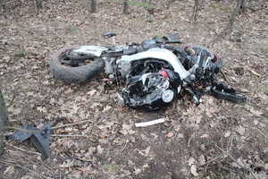 Motocykl lezy na boku na ziemi po wypadku drogowym. Wyraźne ślady uszkodzenia pojazu. Obok porozrzucane elementy motocykla