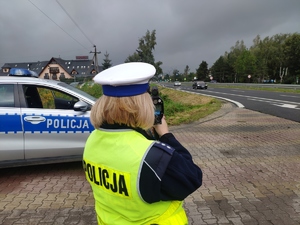 policjantka ruchu drogowego w kamizelce odblaskowej i czapce z białym otokiem mierzy prędkość ręcznym miernikiem prędkości