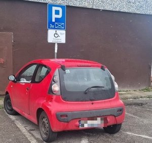 Samochód zaparkowany na miejscu przeznaczonym dla niespełnosprawnych. W tle budynek.