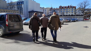 zdj. dwóch policjantów operacyjnych prowadzi przez parking zatrzymanego