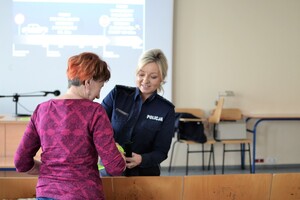 Policjantka ruchu drogowego wręcza starszej kobiecie opaskę odblaskową