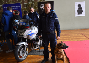 Policyjny przewodnik psa wraz z psem służbowym, obok policyjny motocykl