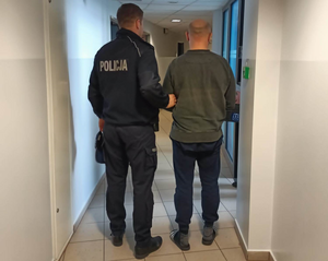 umundurowany policjant prowadzi zatrzymanego przez korytarz komisariatu. Osoby ustawione tyłem do zdjęcia