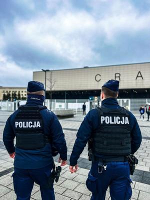 dwóch umundurowanych policjantów stojących tyłem do zdjęcia stojących przed stadionem