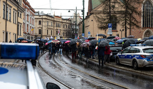 osoby uczestniczące w zgromadzeniu idące jedną z ulic Krakowa. Na zdjęciu widać policyjne radiowozy