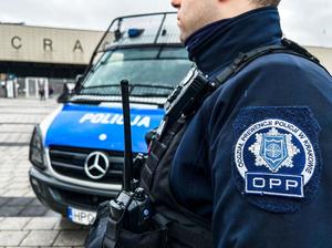 umundurowany policjnt z widaoczną naszywką na ramieniu z napisem Oddział Prewencji Policji w Krakowie stojący przy radiowozie zaparkowanym przy staniodnie