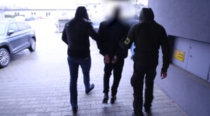 Dwóch policjantów kryminalnych prowadzi przez parking zatrzymanego złodzieja samochodu