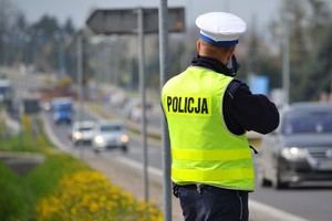 Policjant ruchu drogowego stoi przy krawędzi drogi i mierzy prędkość