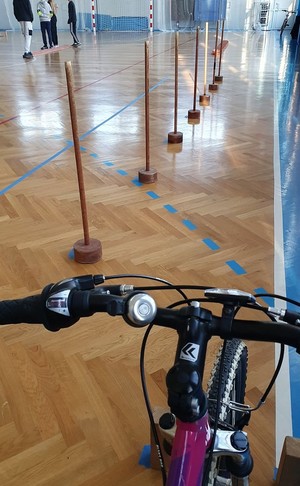 Na zdjęciu widać przednia część rowera i tor przeszkód ustawiony na sali gimnastycznej.