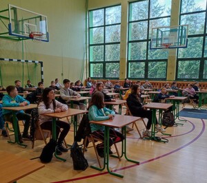 uczniowie siedzą w ławkach na sali gimnastycznej