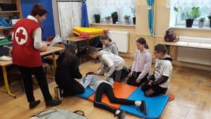 Czworo dzieci pod kontrolą ratownika medycznego udziela pierwszej pomocy dwóm poszkodowanym osobom, z których jedna leży na materacu