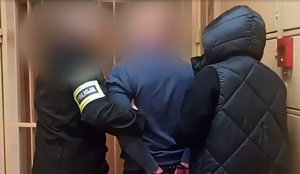 nieumundurowani policjanci prowadzą zatrzymanego, który ma założone kajdanki na ręce trzymane z tyłu