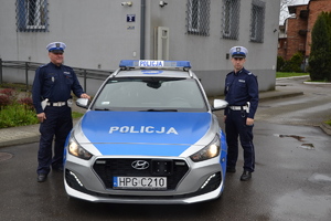 policjanci ruchu drogowego stojący przy oznakowanym radiowozie