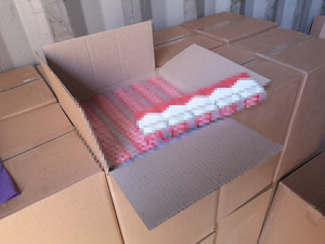 otwarte pudło z widoczną zawartościa nielegalnych paczek papierosów, leżące wśród innych pudeł