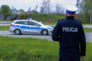 Na pierwszym planie policjant stojący plecami. Przed nim radiowóz na torze