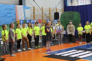 dziewczynka stojąca przed grupą występujących dzieci i trzymająca mikrofon