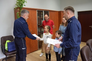 komendant Miejski Policji w swoim gabinecie wraz ze swoim zastępcą wręcza dziewczynce i chłopcu dyplomy