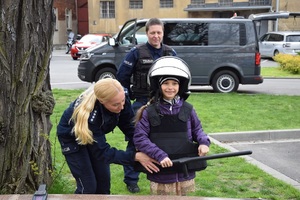 Pani Naczelnik Wydziału Prewencji pomaga przymierzyć dziewczynce elementy umundurowania policjanta zabezpieczającego mecze